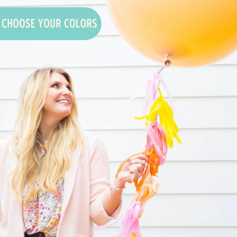 Lady holding a 36 inch balloon in the color blush with pink and yellow tassels on string.