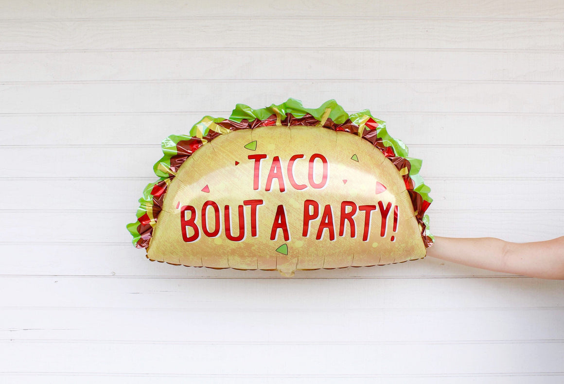 Hand holding a 33 inch jumbo taco balloon with the phrase TACO BOUT A PARTY! in red.