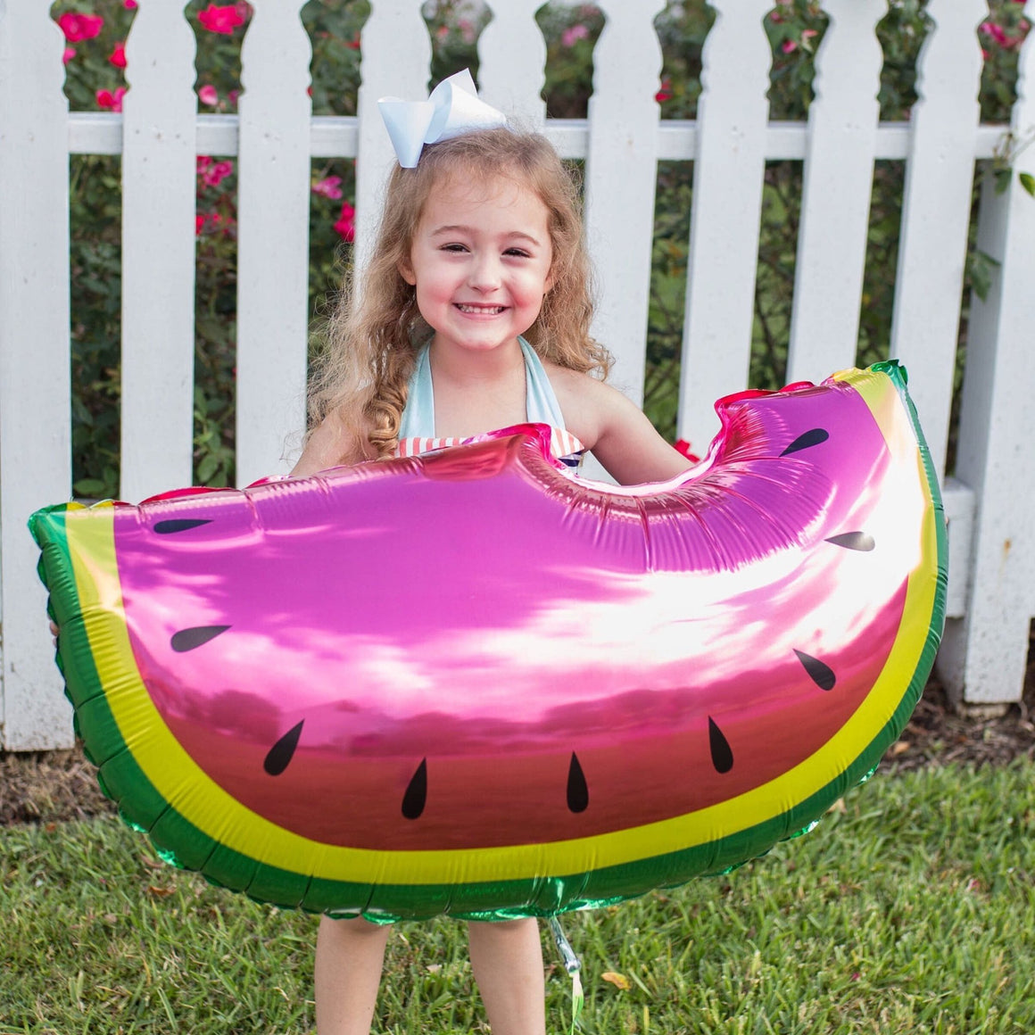 Little girl wearing a white bow with a big smile holding a 35 inch jumbo watermelon fruit balloon.