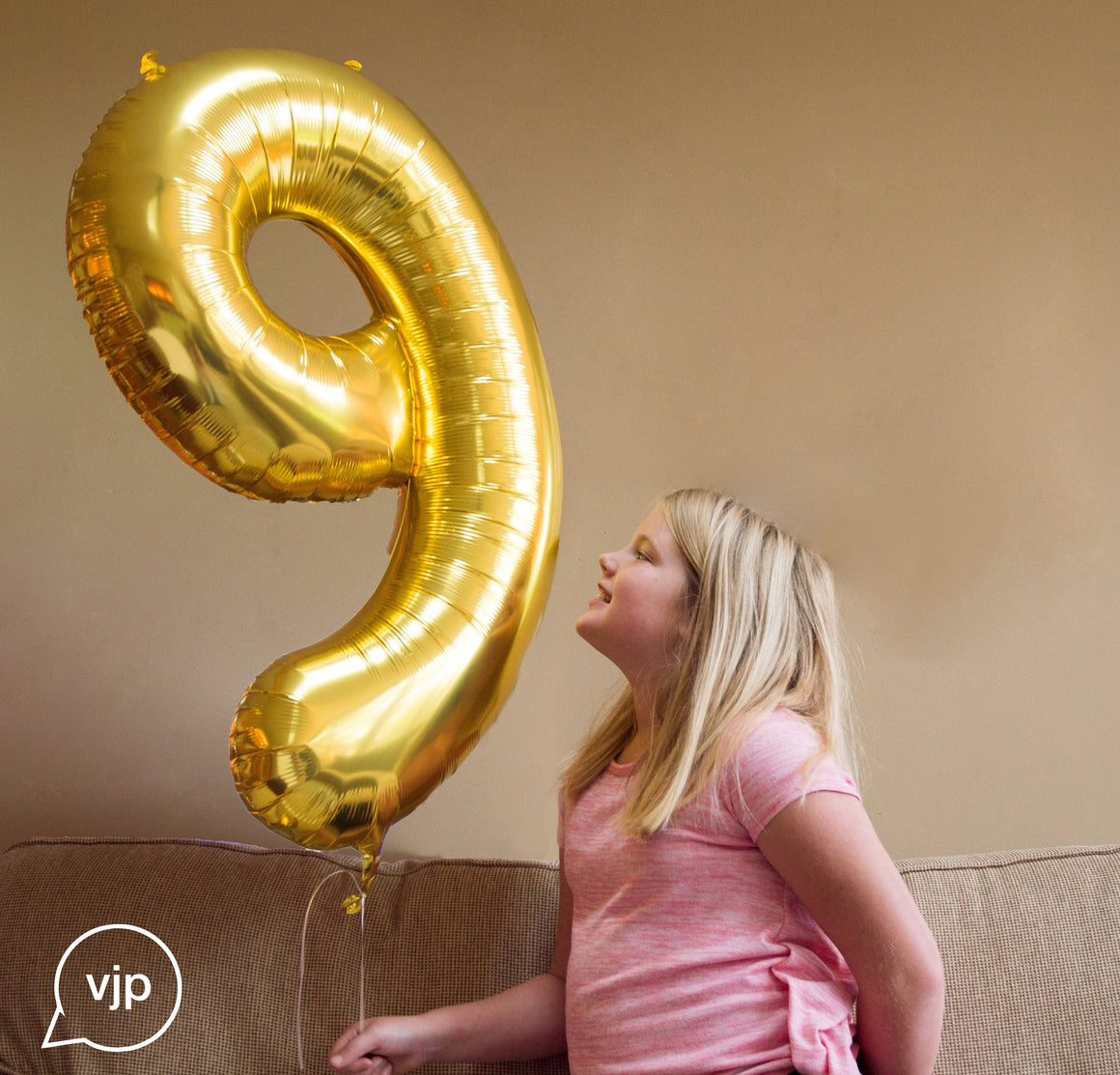 A girl holding and smiling at a helium filled gold number nine balloon.