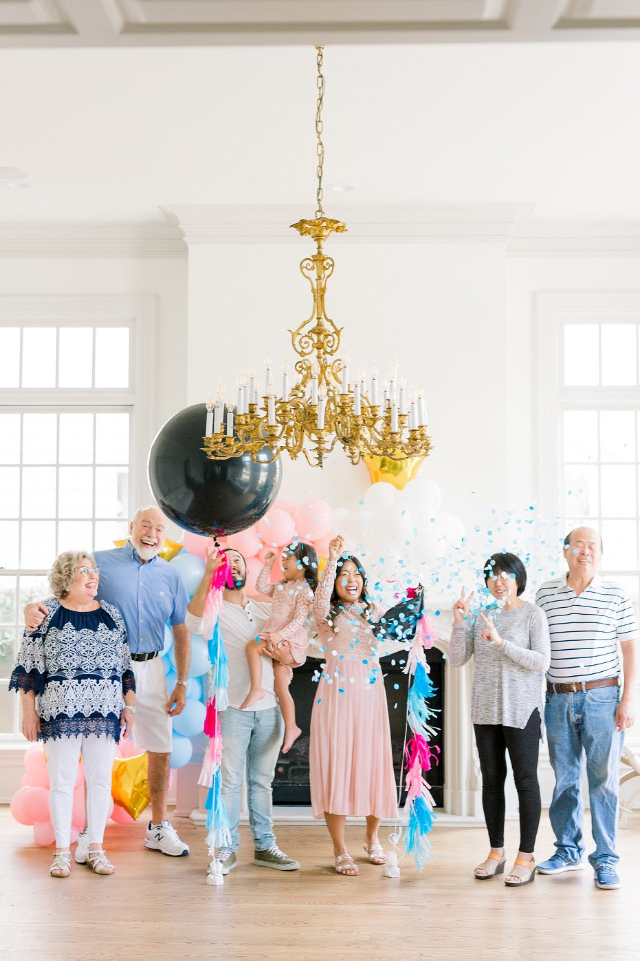 Family celebrating a gender reveal with a black giant balloon filled with either blue or pink confetti.