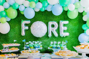 Close up of golf balloon garland in white, lime, spring green, and light blue colors used for golf party decor with table snacks featuring tiny golf decorations.