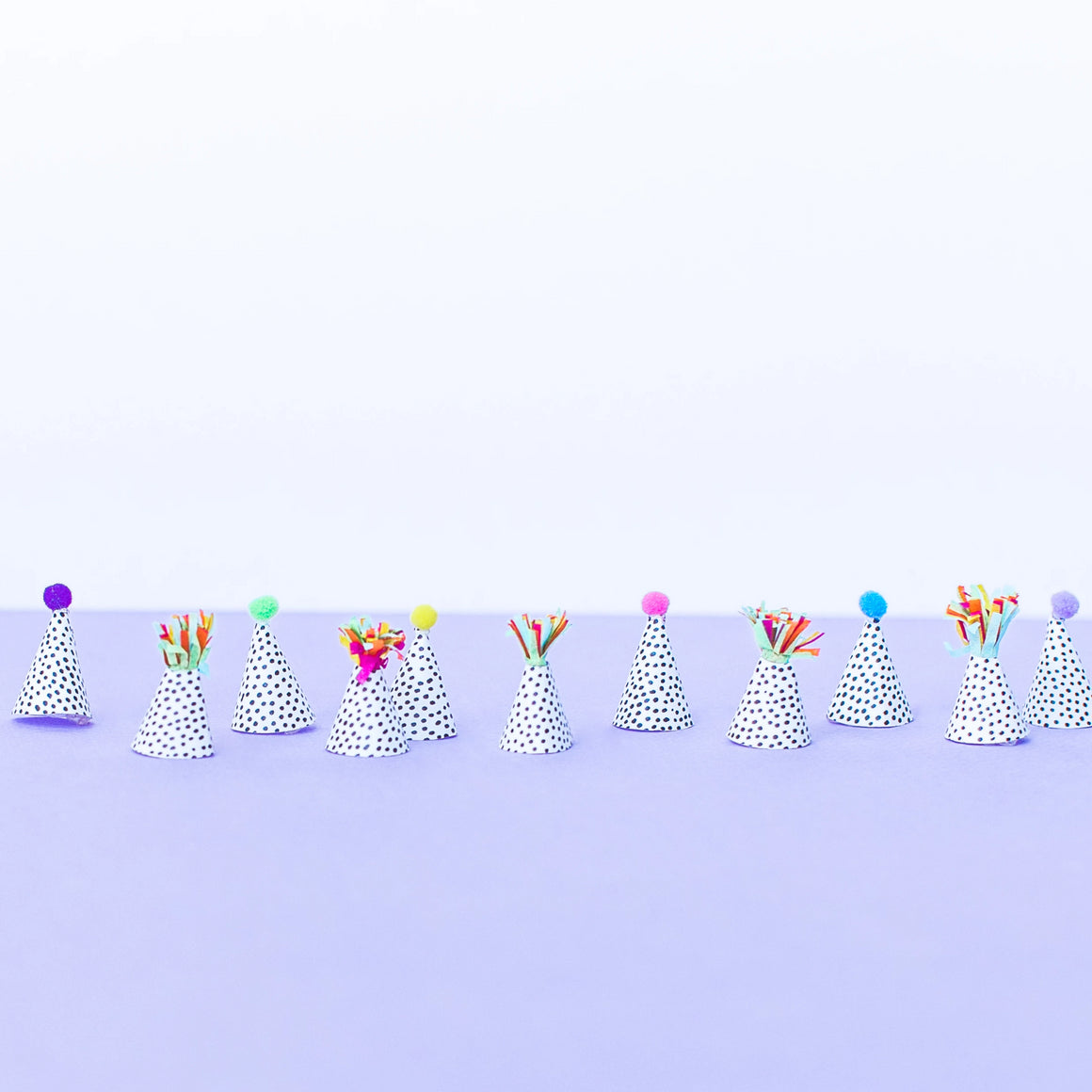 Twelve mini party hats with multi-color fringe and a mix of pom-pom colors used for party decor.