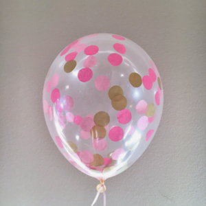 A zoomed up view of a clear latex balloon filled with one inch circular tissue confetti in the colors gold, hot pink, and pink.
