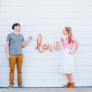 Young couple smiling and holding a cursive rose gold LOVE balloon.