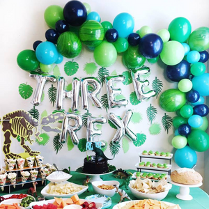 Balloon garland with various balloons in shades of blue and green. There are silver balloons hanging below it that read THREE REX.