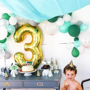 A little boy celebrating his third birthday with cake and a gold number 3 balloon in the background.