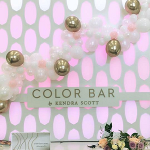 Kendra Scott color bar decorated with a balloon garland in the colors white, light pink, and gold.
