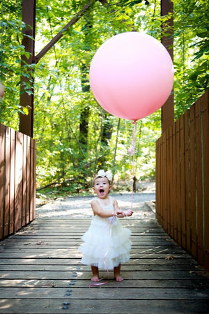 Cute toddler in a white dress holding a jumbo 36 inch pink balloon at the park.