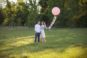 A couple is standing in a grass field and the woman is holding a jumbo 36 inch pink balloon.