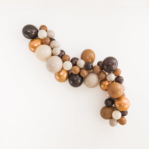 A balloon garland with the colors brown, mocha, tan, double stuffed tan, and copper hangs on a white wall.
