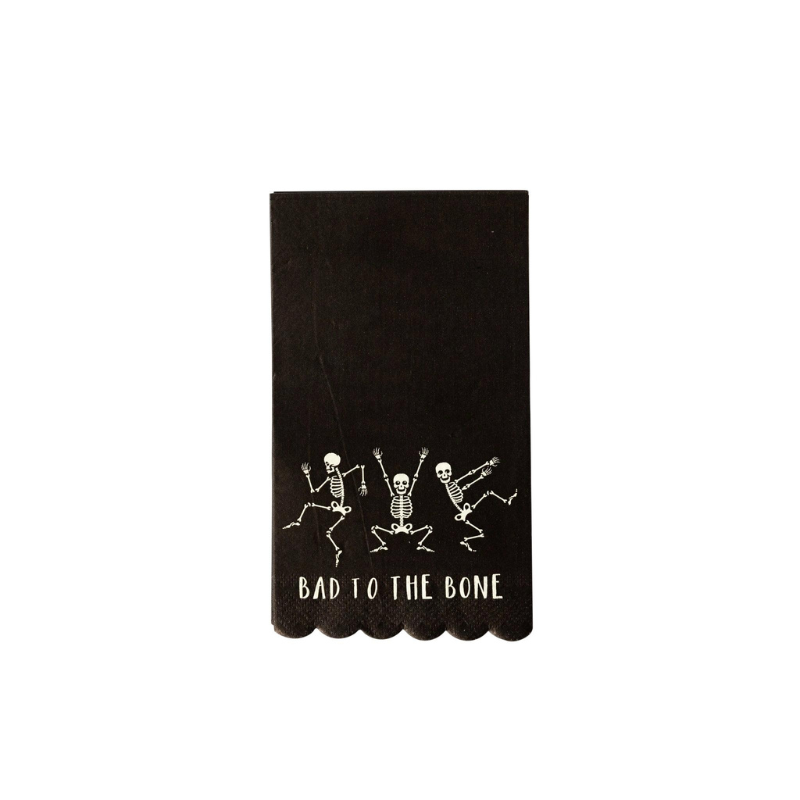 A photo of a black napkin with a scalloped edge. Printed on the napkin are 3 dancing skeletons and the words BAD TO THE BONE.