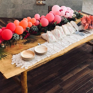 A wood table has a pink and orange balloon garland as a centerpiece.