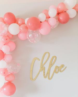 A zoomed in photo shows the pretty balloon garland hanging around the wooden gold child name on the wall.