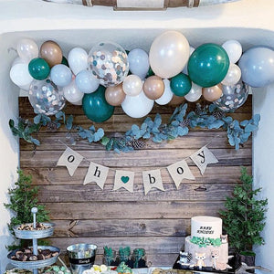 Oh Boy banner hangs from a wood wall with a multicolored balloon garland.