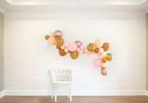 The bachelorette garland is strung on a white wood wall with a white clothe chair sitting in front to help give perspective of the size.