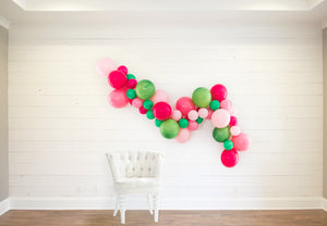 The garland is staged on a white wooden wall with a white cloth chair in front to help show the size of the garland.