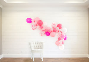 The garland sits on a white wooden wall with a white cloth chair in front.