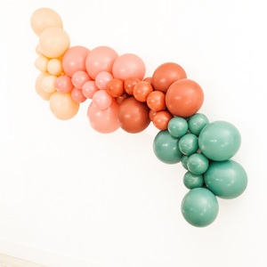 Balloon garland hung on wall with in the colors blush, mauve, terracotta, and willow.