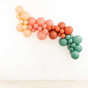 Boho style balloon garland hung on wall with in the colors blush, mauve, terracotta, and willow.