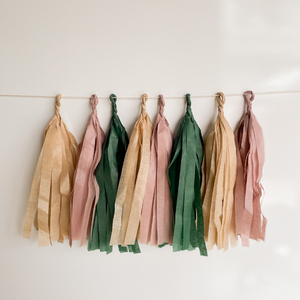 A photo of 8 hand rolled tassles in the colors tan, mauve, and forest green on a white background.