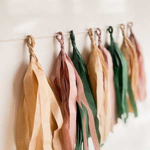 A photo of eight hand rolled tassles in the colors tan, mauve, and forest green on a white background.
