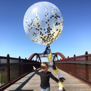 Little boy holding a jumbo 3ft clear balloon filled with tissue confetti in the colors white, black, and yellow with matching balloon string tassels.