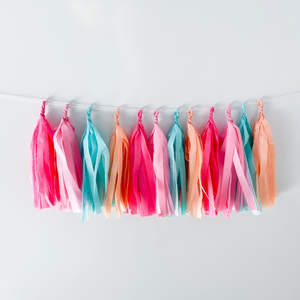 Front view of 12 hand rolled tissue tassels hanging from a white string used as party decor against a white wall.