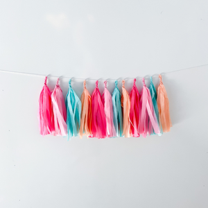 12 hand rolled tissue tassels hanging from a white string used as party decor against a white wall.