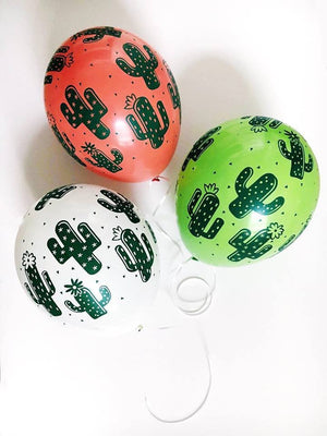 Three latex balloons sit on a white table. All three have green colored cactus designs all over them. One white, one coral, and one lime green balloon.