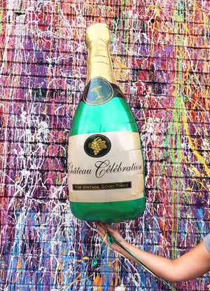 The champagne balloon is held straight up in front of the multicolored streak wall.