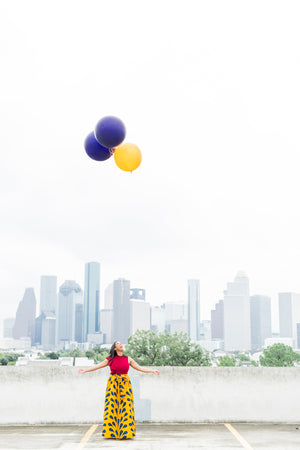 Woman standing in a parking lot is looking up as three jumbo balloons float away.