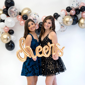 Two girls smiling holding a 46 inch gold mylar "cheers" balloon.