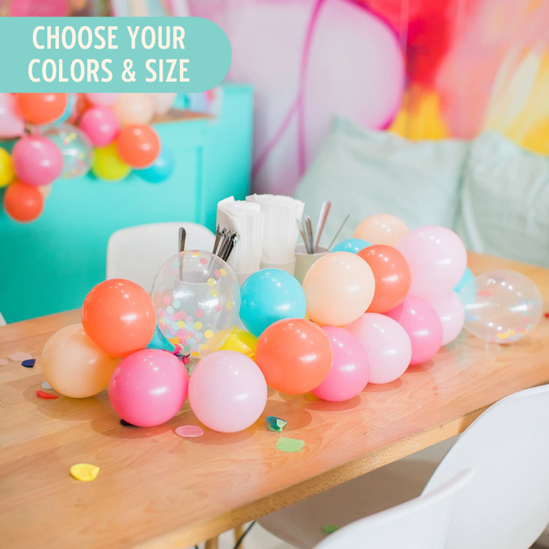 A bright mini balloon garland made up of only 5 inch balloons sits running along the top of a wooden table. The colors are coral, rose, blush, Caribbean blue, wildberry, yellow, and matching clear filled confetti balloons.