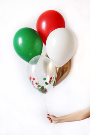 A hand holding a chrismas balloon bundle with five balloons; one red, one green, one white, one gold, and one clear filled matching color confetti.
