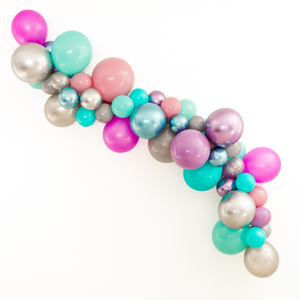 A balloon arch garland with the following colors: chrome silver, chrome purple, chrome blue, caribbean blue, aquamarine, spring lilac, gray, silver, soft plum, and neon purple is hung on the wall at a party celebration.