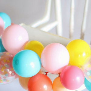 Mini balloon garland wrapped around a white high chair.