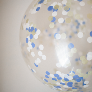 Close up of giant 3ft clear balloon stuffed with tissue confetti in the colors blue, white, and gold.