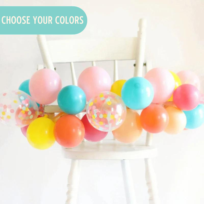 Mini balloon garland wrapped around a white high chair.