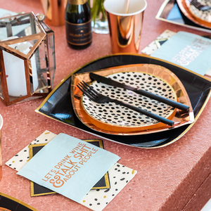 Black dot cream colored plate sits on top of a gold foil paper plate in a tablescape setting.