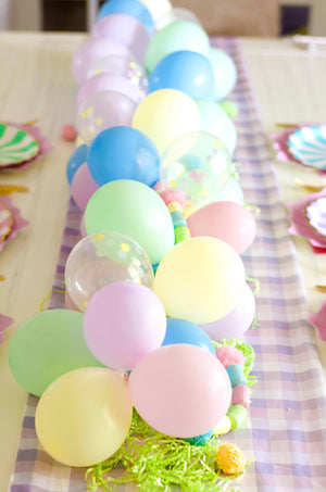 A mini balloon garland with pastel colors sits on a table as a centerpiece.