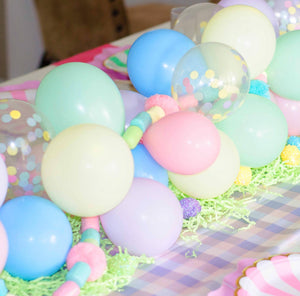 Cute tablescape with pastel colored mini balloon garland used as a centerpiece with pastel colored paper plates on the table and gold forks.