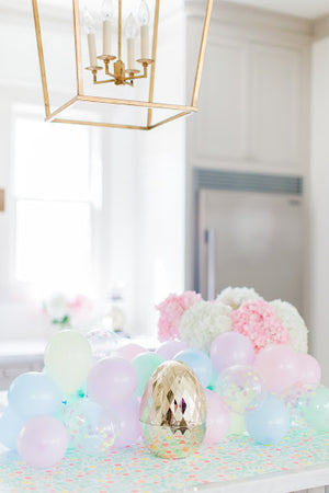 A mini pastel balloon garland sits on a counter with a gold Easter egg in front of it.