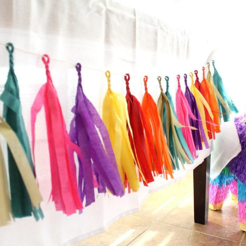 A tassel garland with the colors hot pink, purple, yellow, red, orange, gold, and teal hangs from a white table.