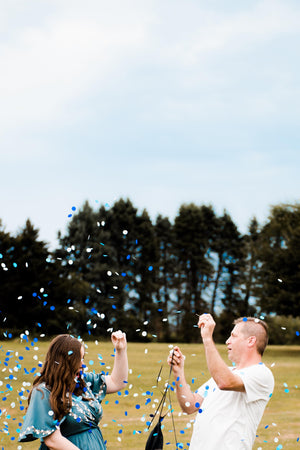 Gender reveal couple popping a 36 inch black latex balloon filled with shades of blue confetti.
