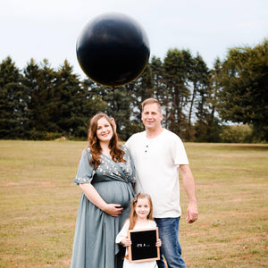Gender reveal couple holding a 36&quot; black latex balloon filled with shades of either blue for boy or pink for girl confetti.