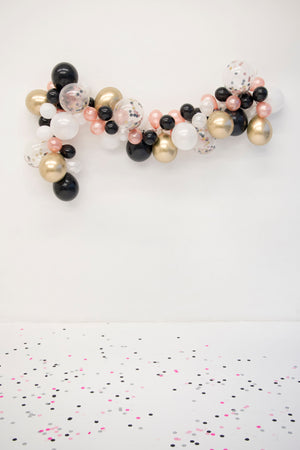 A zoomed out view of the garland reveals the white floor that has one inch tissue confetti circles scattered all over the floor in white, black, rose gold, and chrome gold colors.