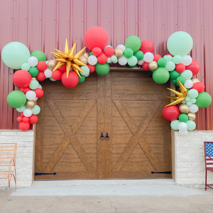 Christmas theme balloon arch garland with red, white, green, and gold balloons in various sizes. The balloon garland has two jumbo gold starburst balloons.