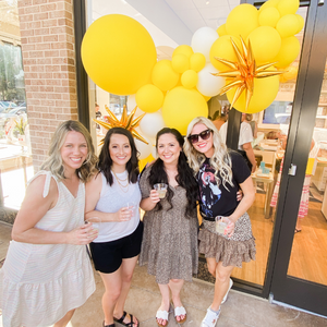 Four woman stand in front of a balloon garland with balloons colored yellow and white and jumbo gold starburst balloons at a Kendra Scott jewelry store.