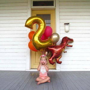 Little girl sitting on a porch in front of a 34 inch gold mylar number two balloon.